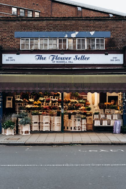 The exterior of 'The Flower Seller' florist shop in Muswell Hill, displaying a variety of fresh flower bouquets and floral arrangements arranged on white wooden shelves and tables outside the large gl